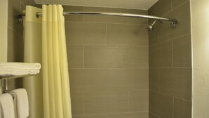 A shower area with beige tiles, a yellow shower curtain, and a metal shower head. - Valley Inn Shakopee (Shakopee)