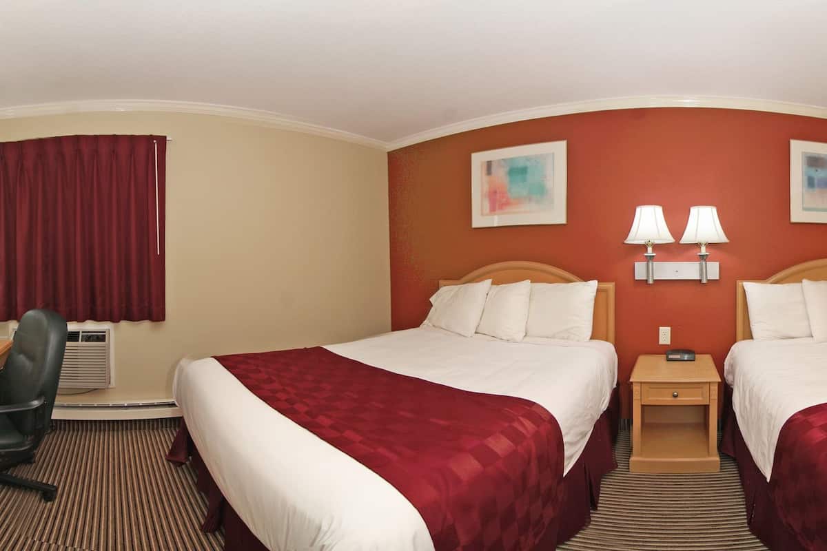 Habitación de hotel con dos camas, un escritorio con televisor, armario y baño.