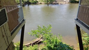 A view of a river from a balcony with a wooden railing, surrounded by greenery and a stone wall. - RoseWood Inn (Bryson City)