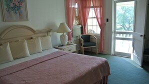 A bedroom with a bed, bedside table, lamp, chair, and a view of the outdoors. - RoseWood Inn (Bryson City)