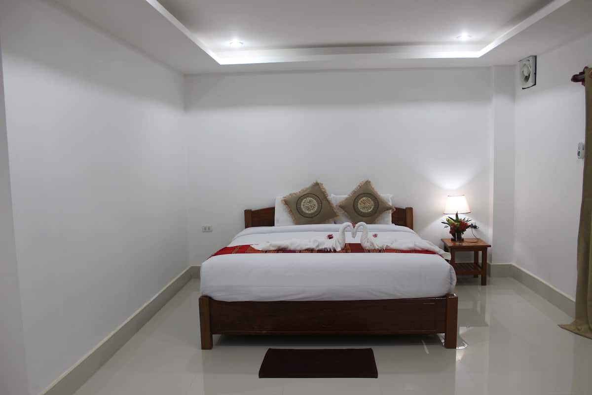 A neatly made bed with white linens and decorative pillows, a bedside table with a lamp, and a small plant.