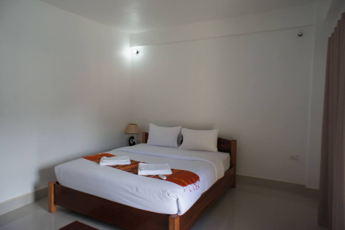A neatly made bed with white linens and an orange throw blanket, a bedside lamp, and a wooden headboard.