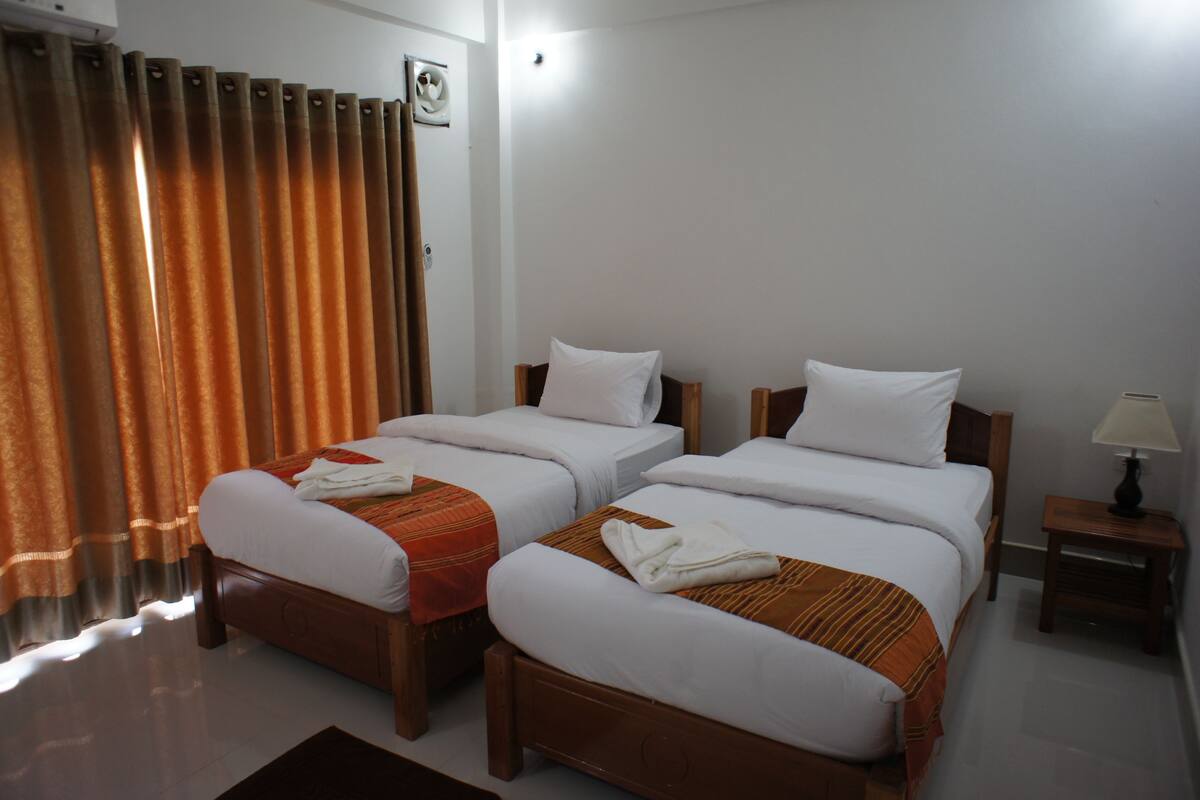 A hotel room with two single beds, a nightstand with a lamp, and a window with curtains.