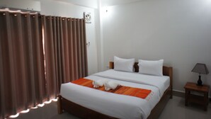 Una camera d'albergo con un letto grande, un comodino con una lampada e una finestra con tende.