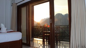 Una camera d'albergo con un letto, un balcone con tavolo e sedie, e vista sulle montagne.