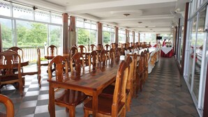Un lungo tavolo da pranzo con sedie di legno in una stanza spaziosa con ampie finestre e un pavimento a scacchi.