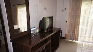 Quarto com escrivaninha de madeira, televisão e janela com cortinas.