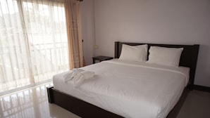 Uma cama bem arrumada com lençóis brancos e cabeceira escura em um quarto com uma janela grande e uma pequena mesa de cabeceira.