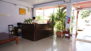 Uma área de recepção com balcão de madeira, uma cadeira, um vaso de planta e uma janela ampla com vista para o exterior.