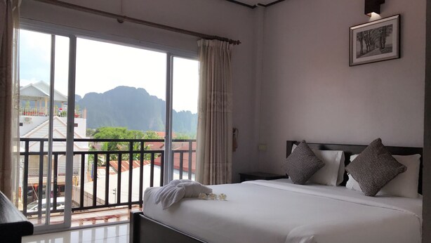 Quarto de hotel com uma cama grande, vista para as montanhas e uma varanda com guarda-corpo.
