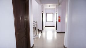 Corredor com porta de madeira, um extintor e uma janela no final.