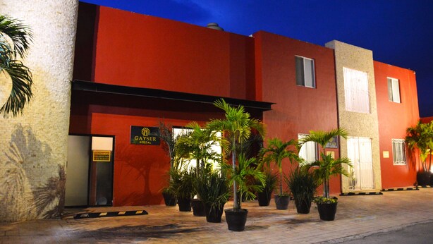 A building with a red facade, a sign reading "GAYSER HOSTAL", and several potted plants in front. - Gayser Apartamentos (Valladolid)