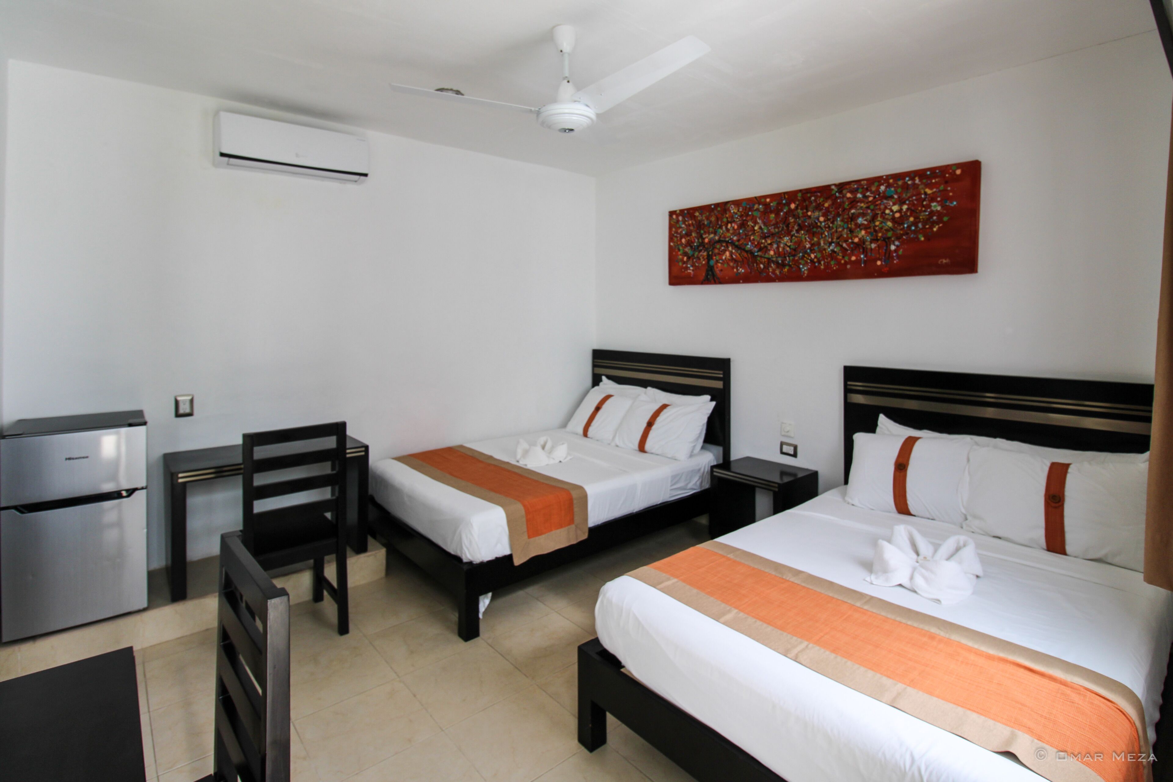 A hotel room with two beds, a desk, a chair, an air conditioning unit, and a ceiling fan.