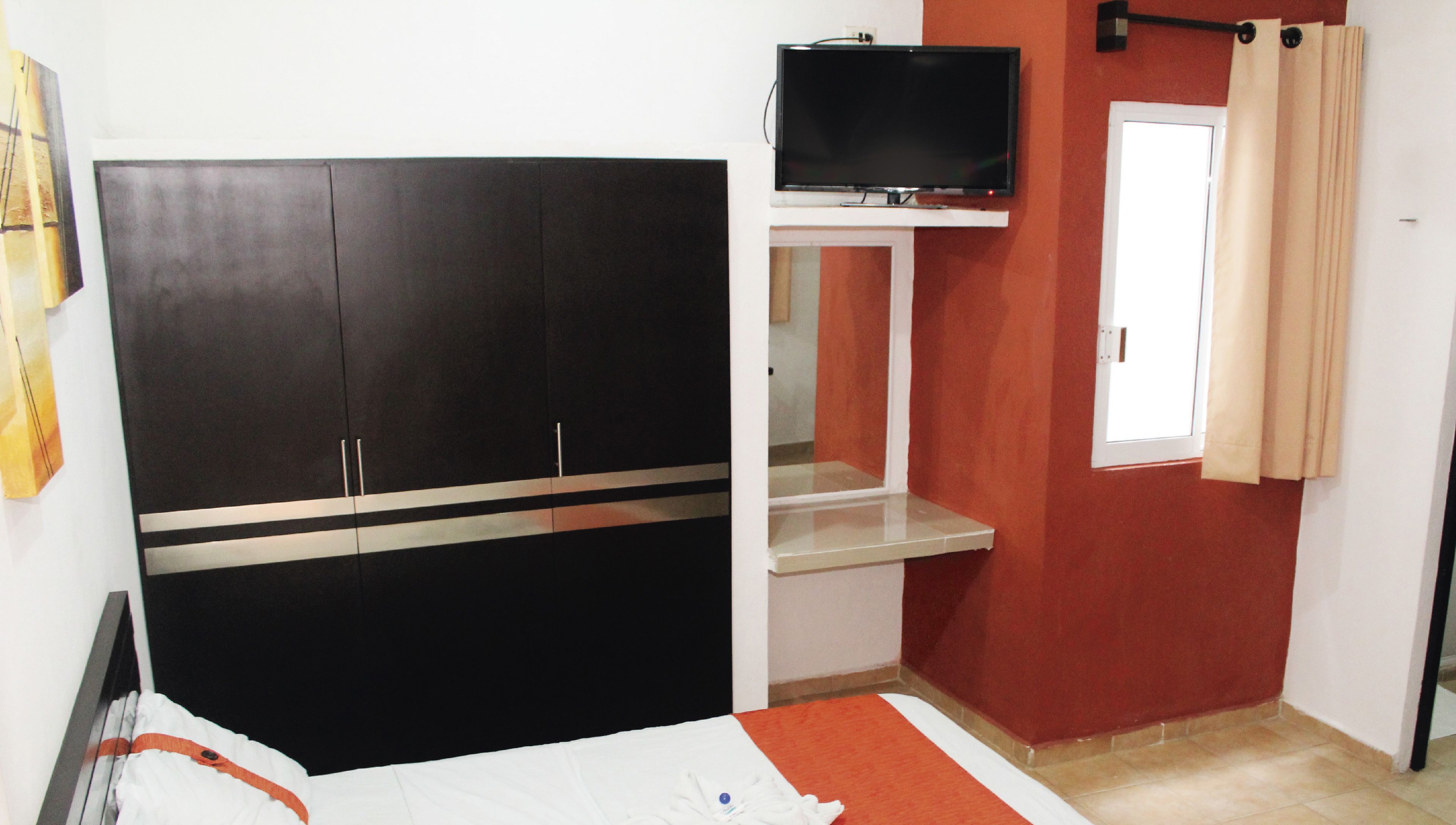 Una camera da letto con un letto, un armadio, una televisione e una finestra con tende.