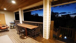 En overdækket terrasse med et træbord og stole, store vinduer og et gelænder.