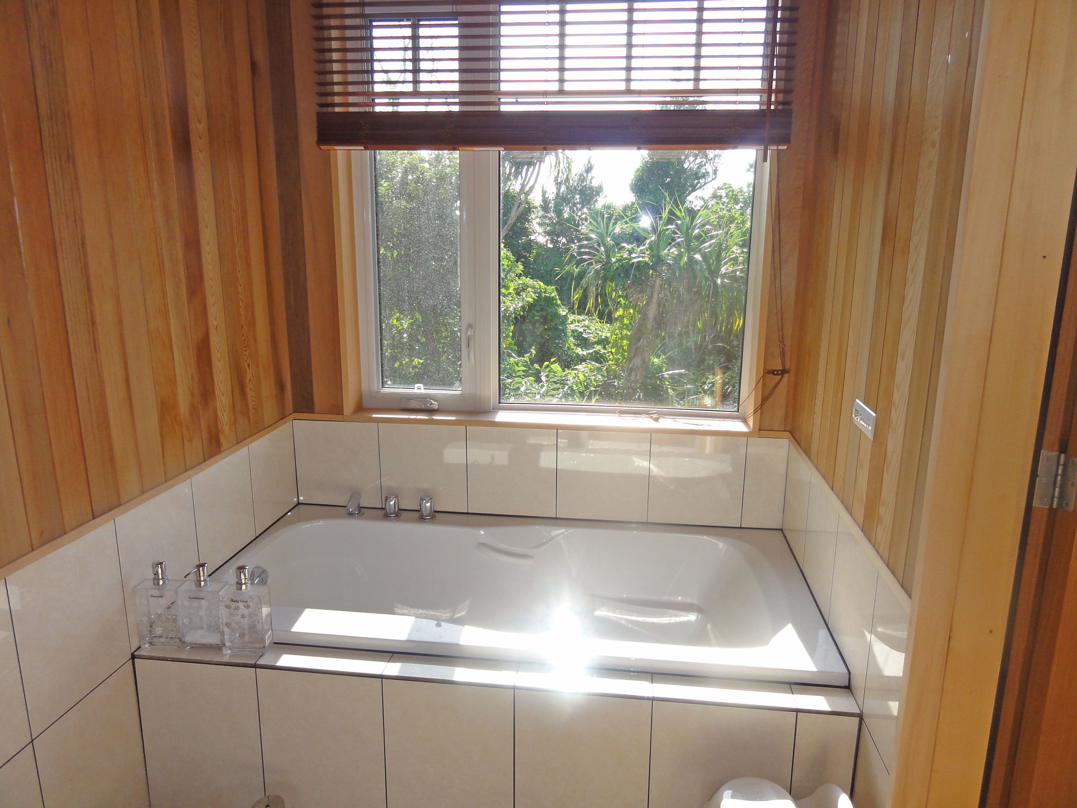 Une salle de bain au décor intérieur en bois, avec une grande baignoire et une fenêtre donnant sur un paysage verdoyant.
