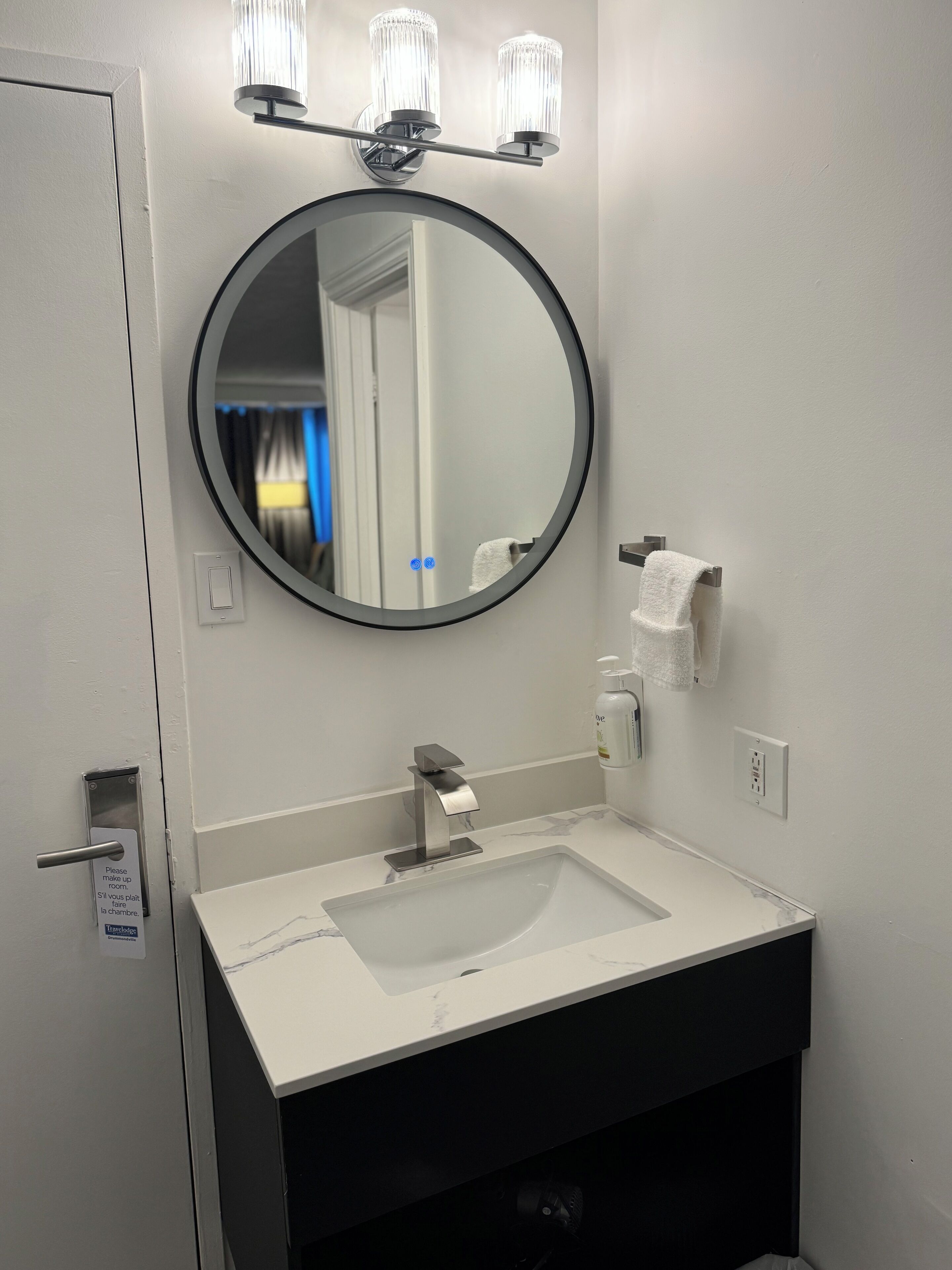 A bathroom with a round mirror, a sink, a towel rack, and a soap dispenser.
