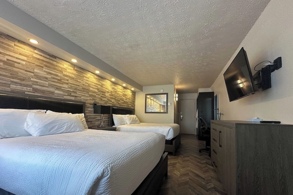Habitación de hotel con dos camas, un escritorio, un televisor y suelo con estampado de espiga.