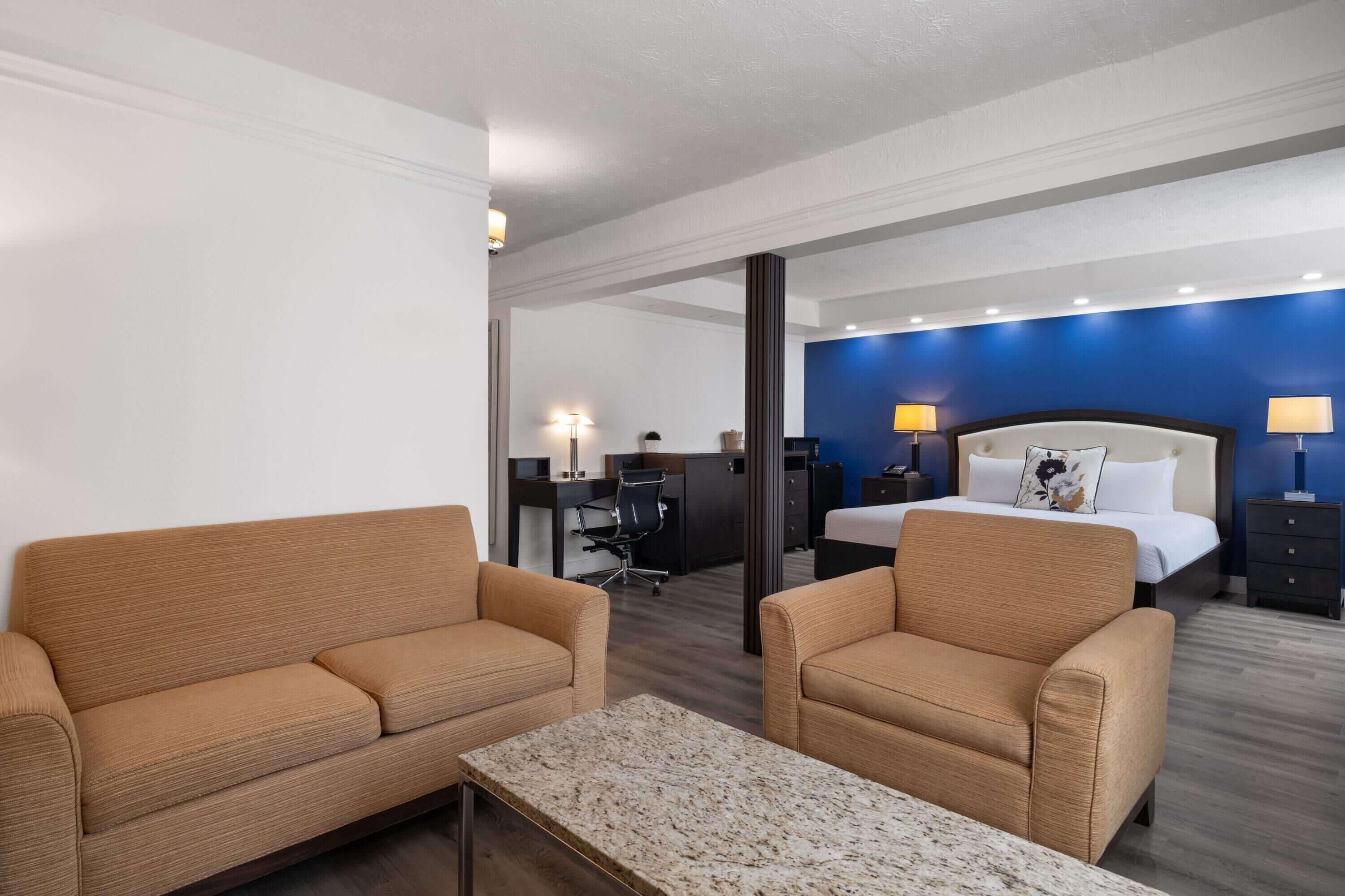 Una habitación de hotel con una cama, dos sillones, un escritorio y una mesita.