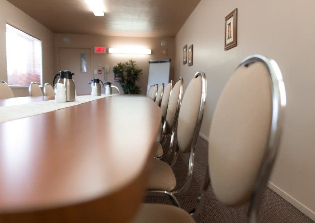 A conference room with a long table, chairs, and a coffee pot.