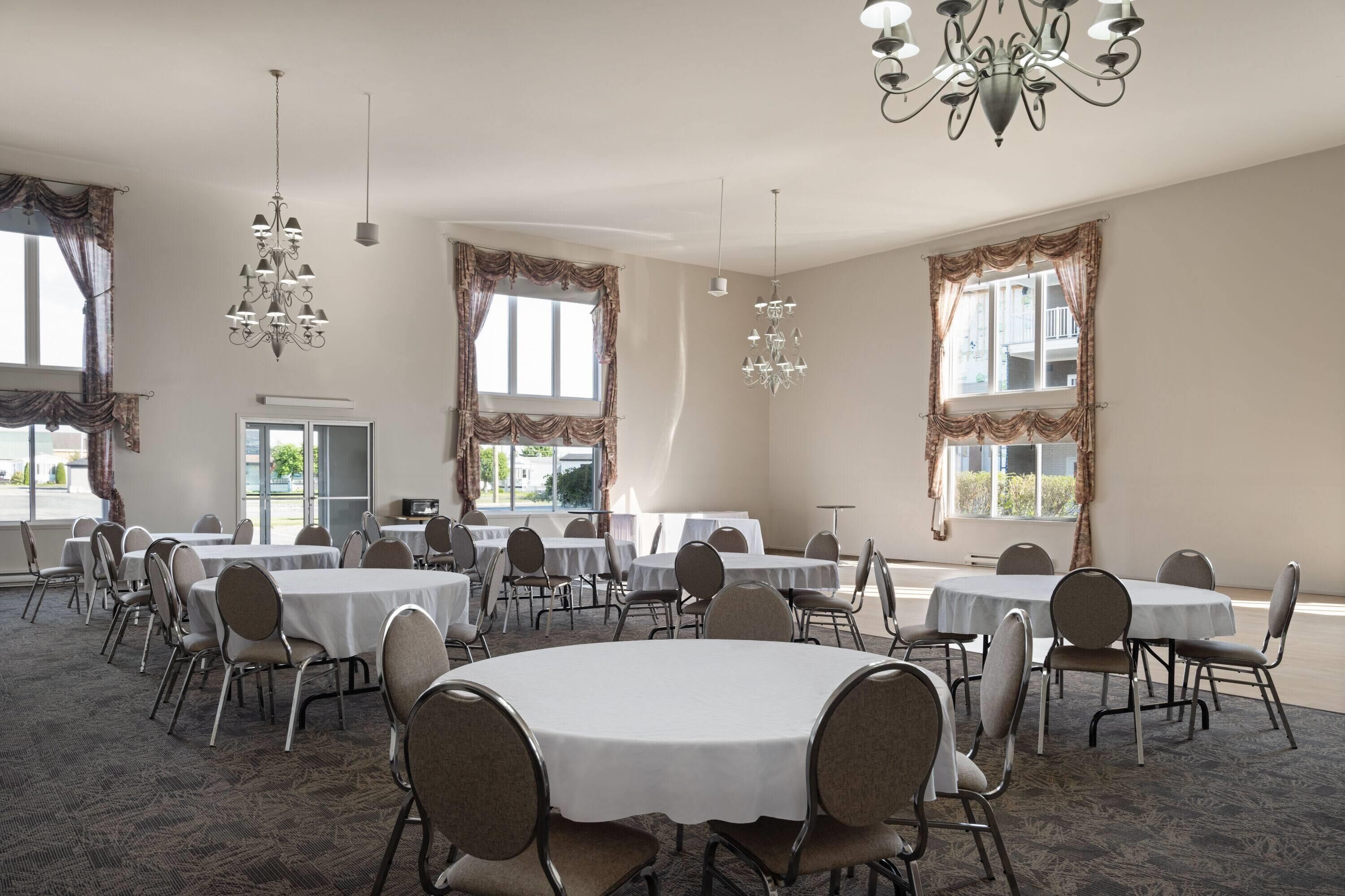 Een vergaderzaal met ronde tafels, stoelen, kroonluchters en grote ramen voorzien van gordijnen.