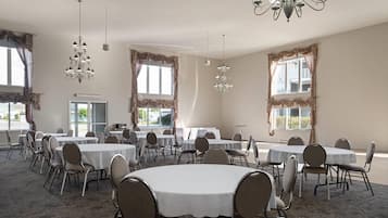 Een vergaderzaal met ronde tafels, stoelen, kroonluchters en grote ramen voorzien van gordijnen.