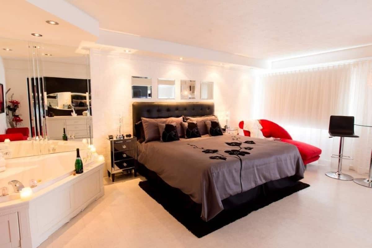 Quarto moderno com uma cama grande, banheiro separado com banheira e uma cadeira vermelha.