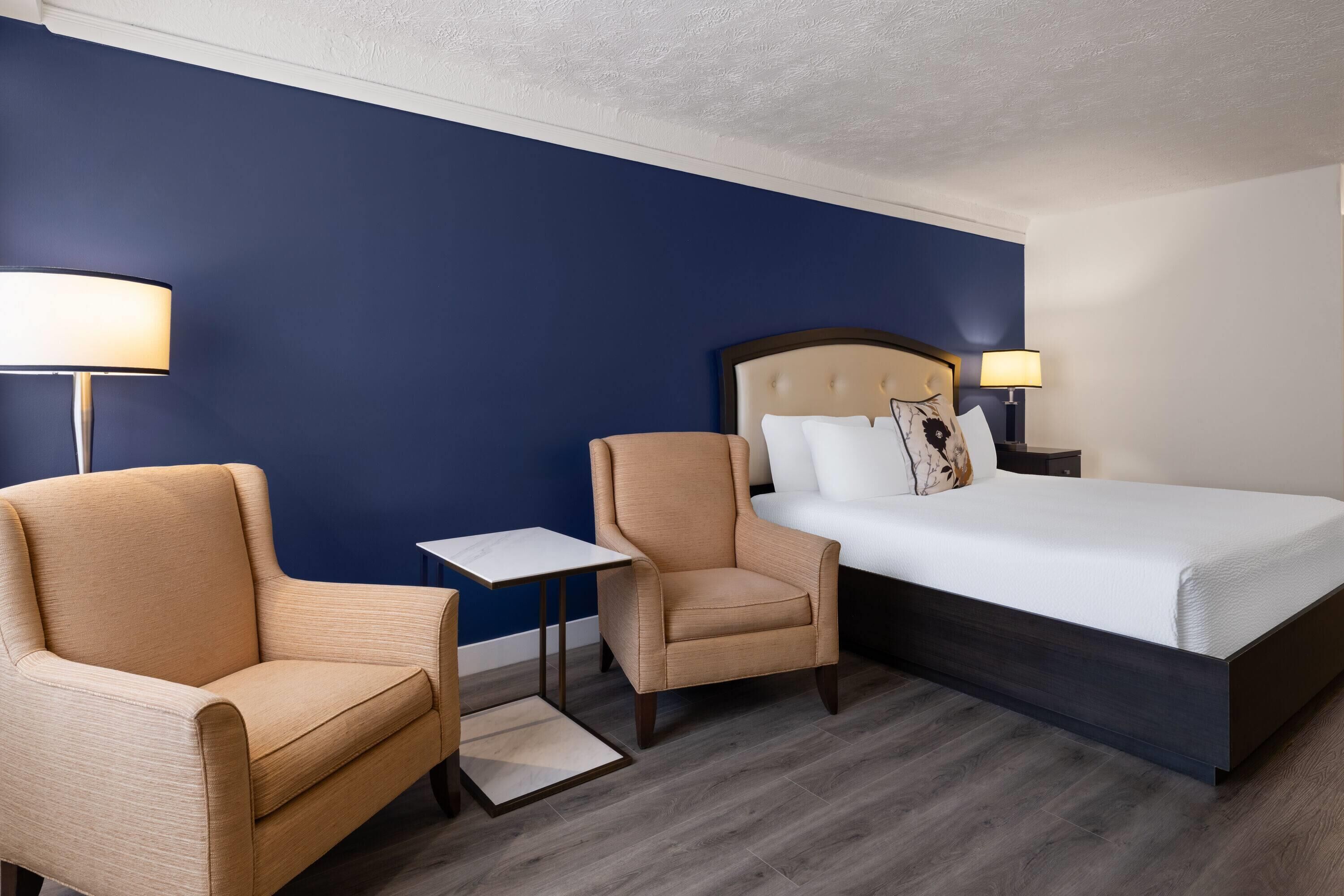 A hotel room with a bed, two armchairs, a small table, and two bedside lamps.