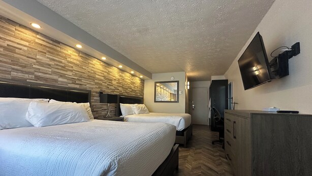 Une chambre d’hôtel avec deux lits, un téléviseur fixé au mur, une tête de lit en bois et un parquet à motifs en chevrons.