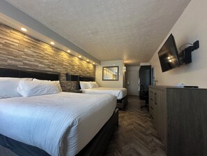 Habitación de hotel con dos camas, un televisor montado en la pared, cabecera de madera y suelo con estampado de espiga.