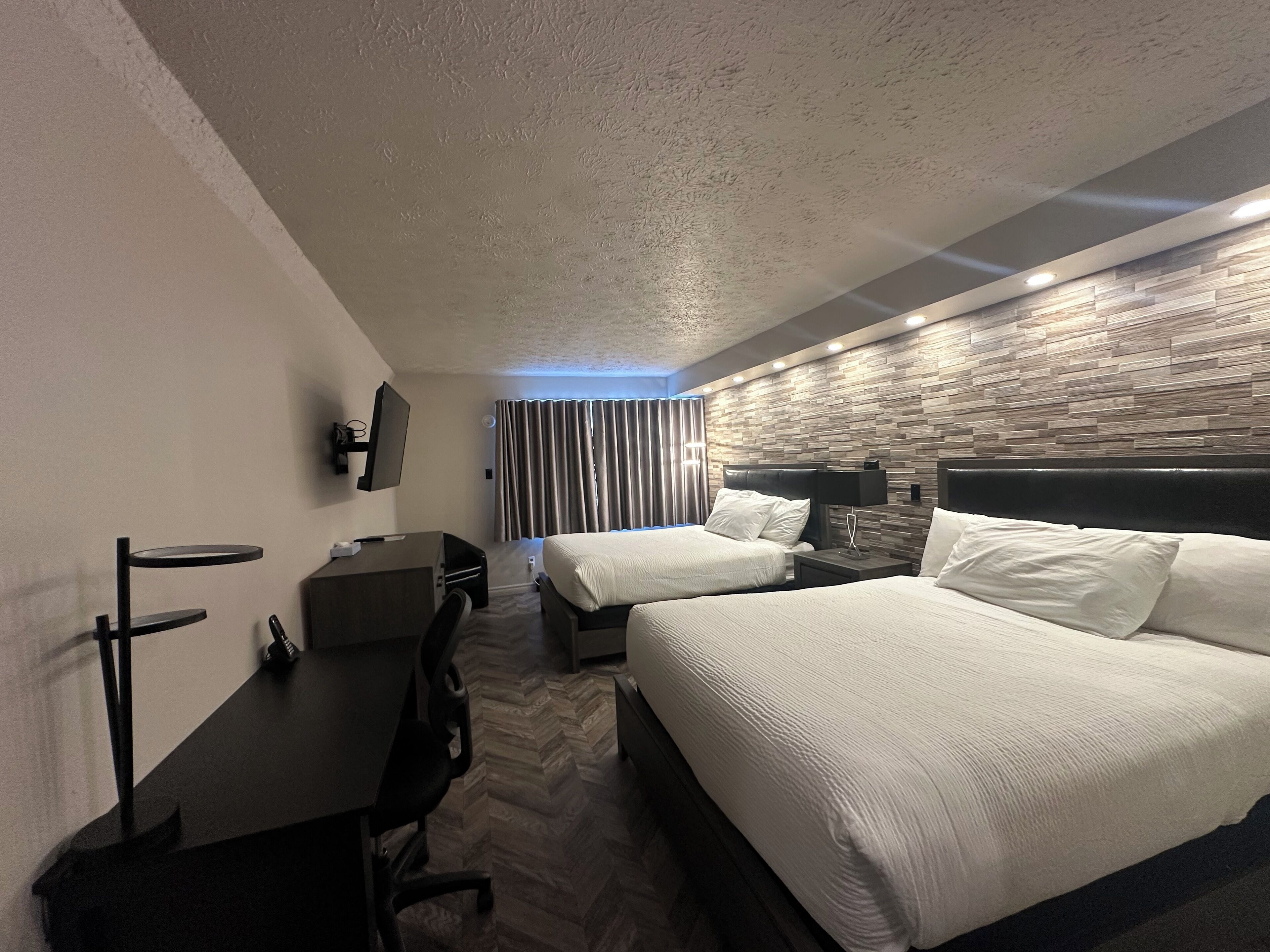 A hotel room with two beds, a desk, a chair, a TV, and a wall with a textured pattern.