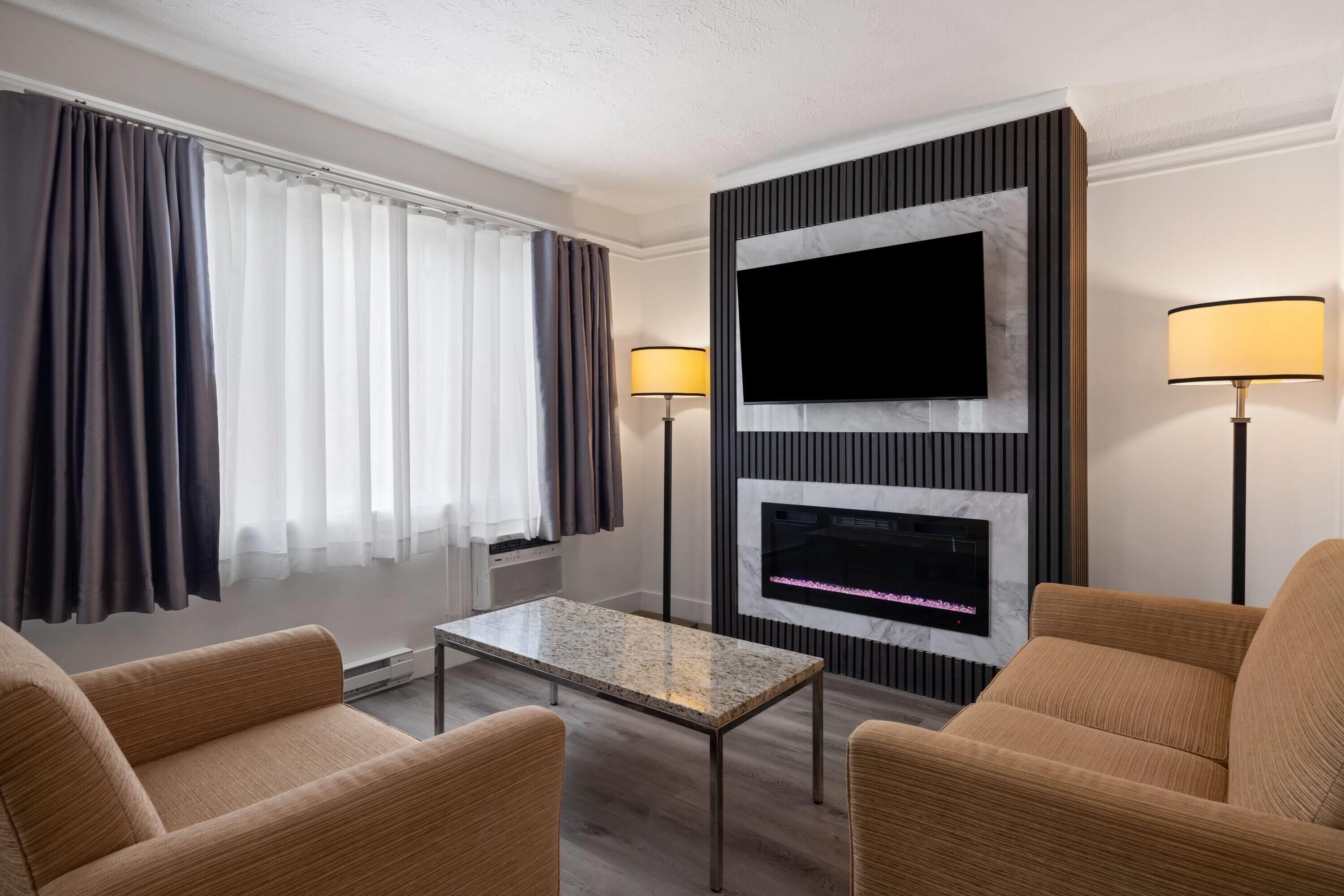 A hotel room with a flat-screen TV, a fireplace, two lamps, a coffee table, and two sofas.