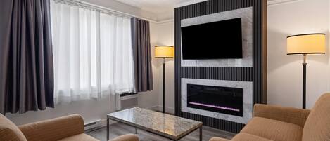 A hotel room with a flat-screen TV, a fireplace, two lamps, a coffee table, and two sofas.