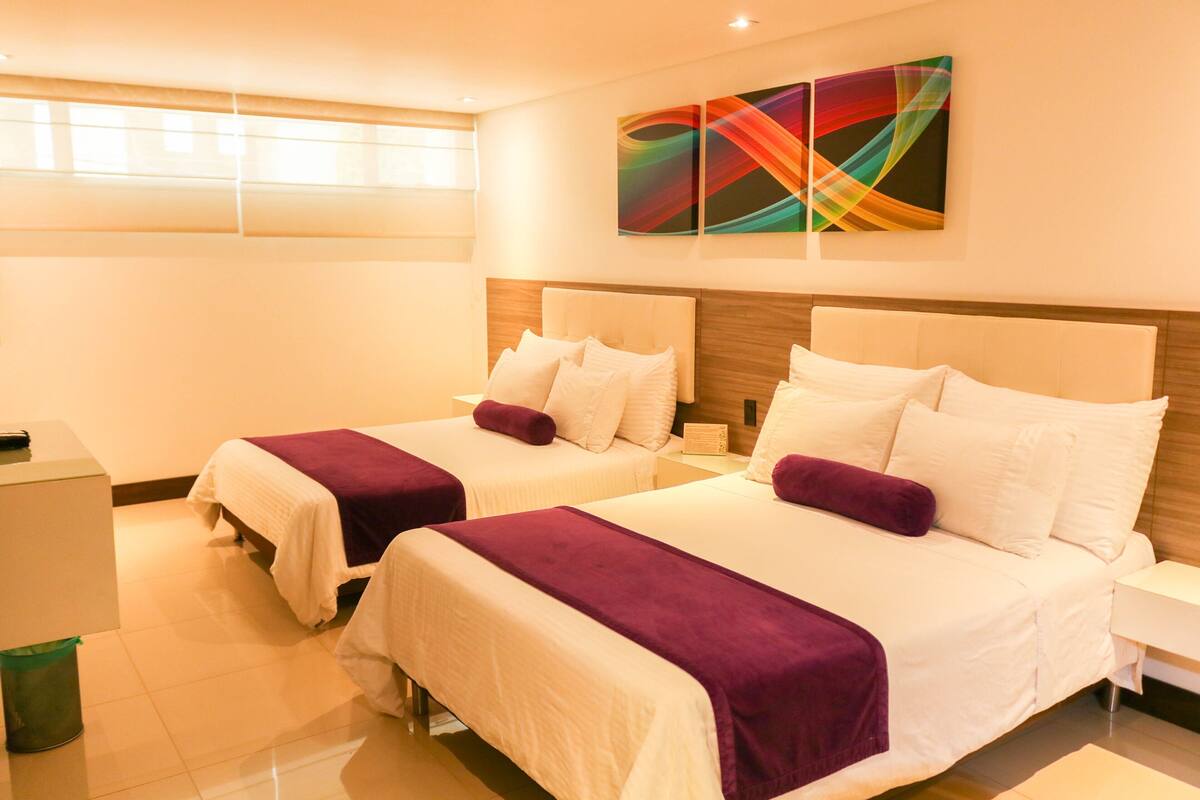 A hotel room with two beds, each with a headboard, a bedside table, and a wall-mounted artwork.