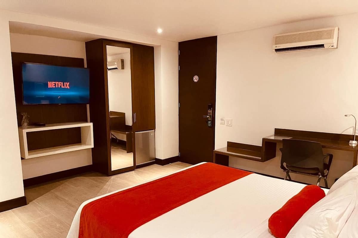 A hotel room with a large bed, a TV mounted on the wall, a desk, and a chair.