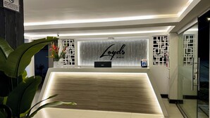Zona de recepción de un hotel con diseño moderno, que incluye un mostrador de recepción, un letrero que dice "Loyds Hotel" y una planta decorativa.