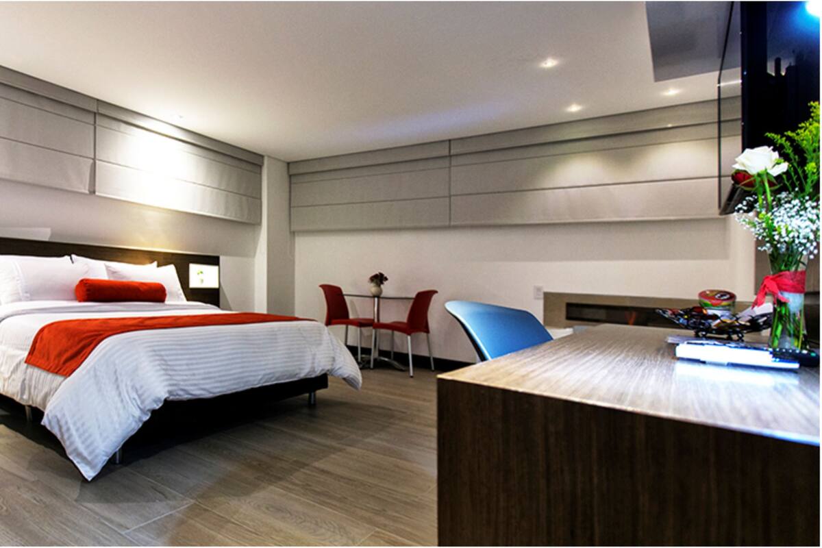 A modern hotel room with a large bed, bedside tables, a desk, and a chair.