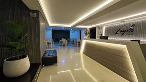 Zona de recepción de un hotel con diseño moderno, que incluye un mostrador de recepción, un área de estar y una planta en maceta.