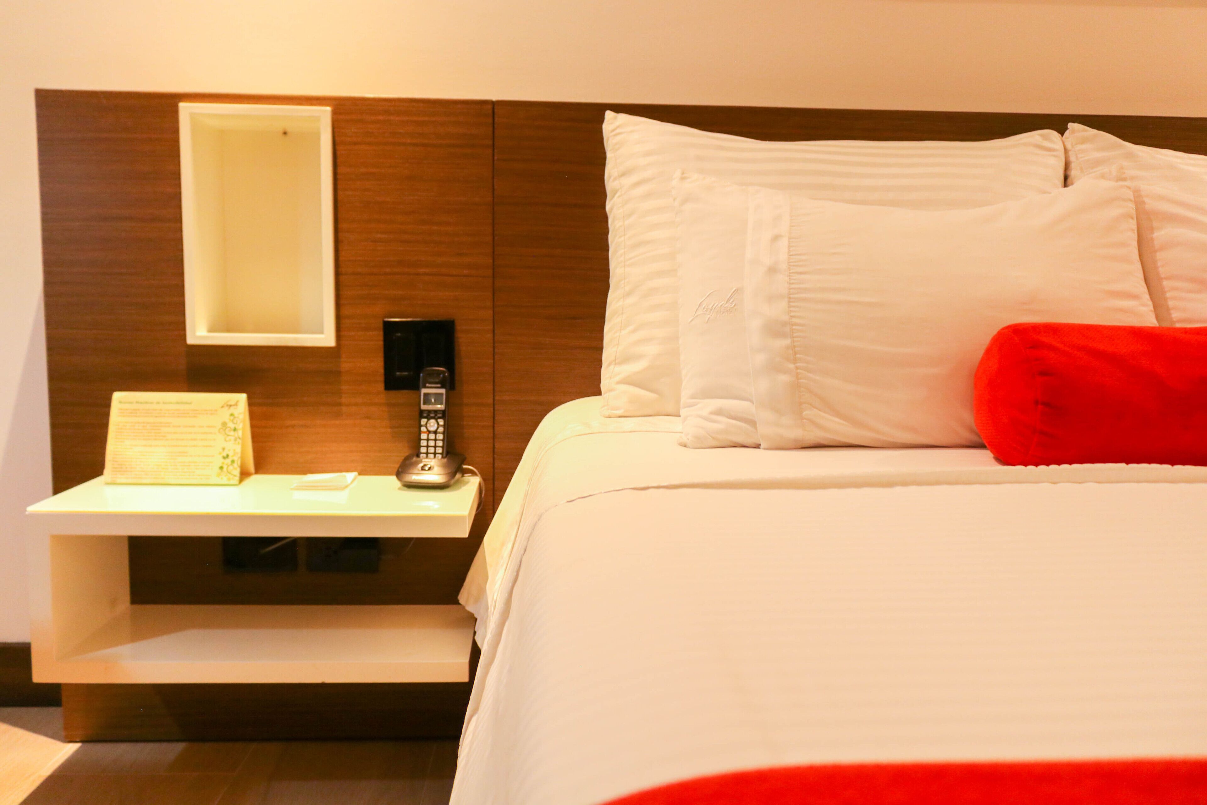 A hotel room with a bed, a nightstand, a telephone, and a mirror.