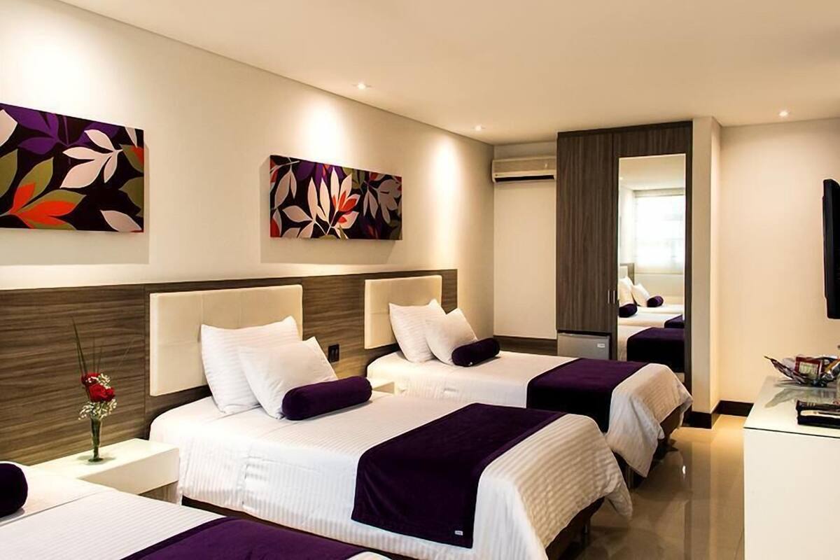 A hotel room with two beds, a desk, and artwork on the walls.
