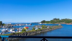 A marina with boats docked, a small house with a red roof, and a rocky shoreline with trees. - Glen Lyon Inn & Suites (Port Hardy)