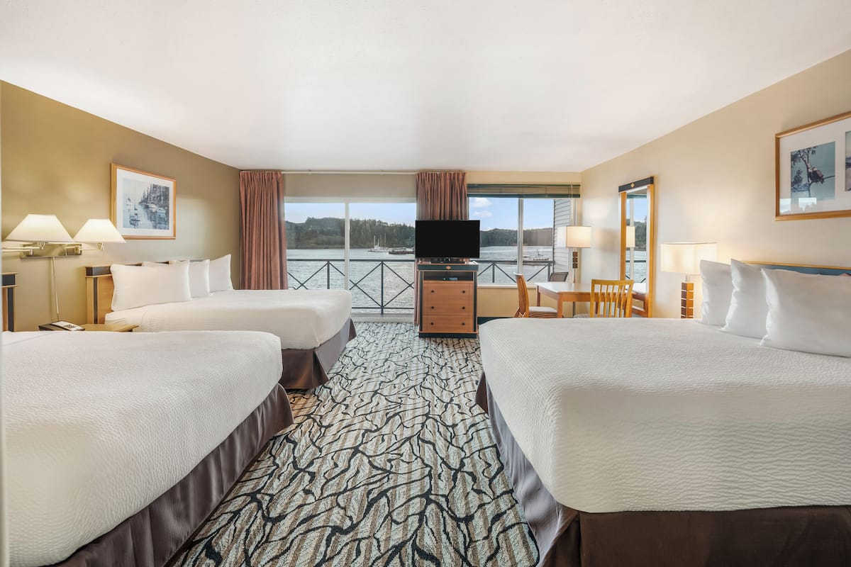 A hotel room with two beds, a TV, a desk, and a view of the water.