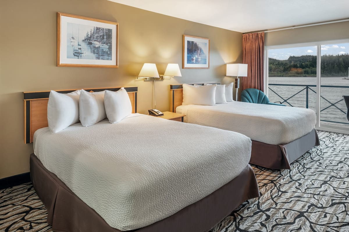 A hotel room with two beds, a large window with a view of a body of water, and two wall-mounted lamps.
