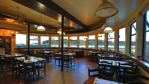 A spacious restaurant with high ceilings, large windows offering views of a lake and hills, and multiple dining tables and chairs. - Glen Lyon Inn & Suites (Port Hardy)