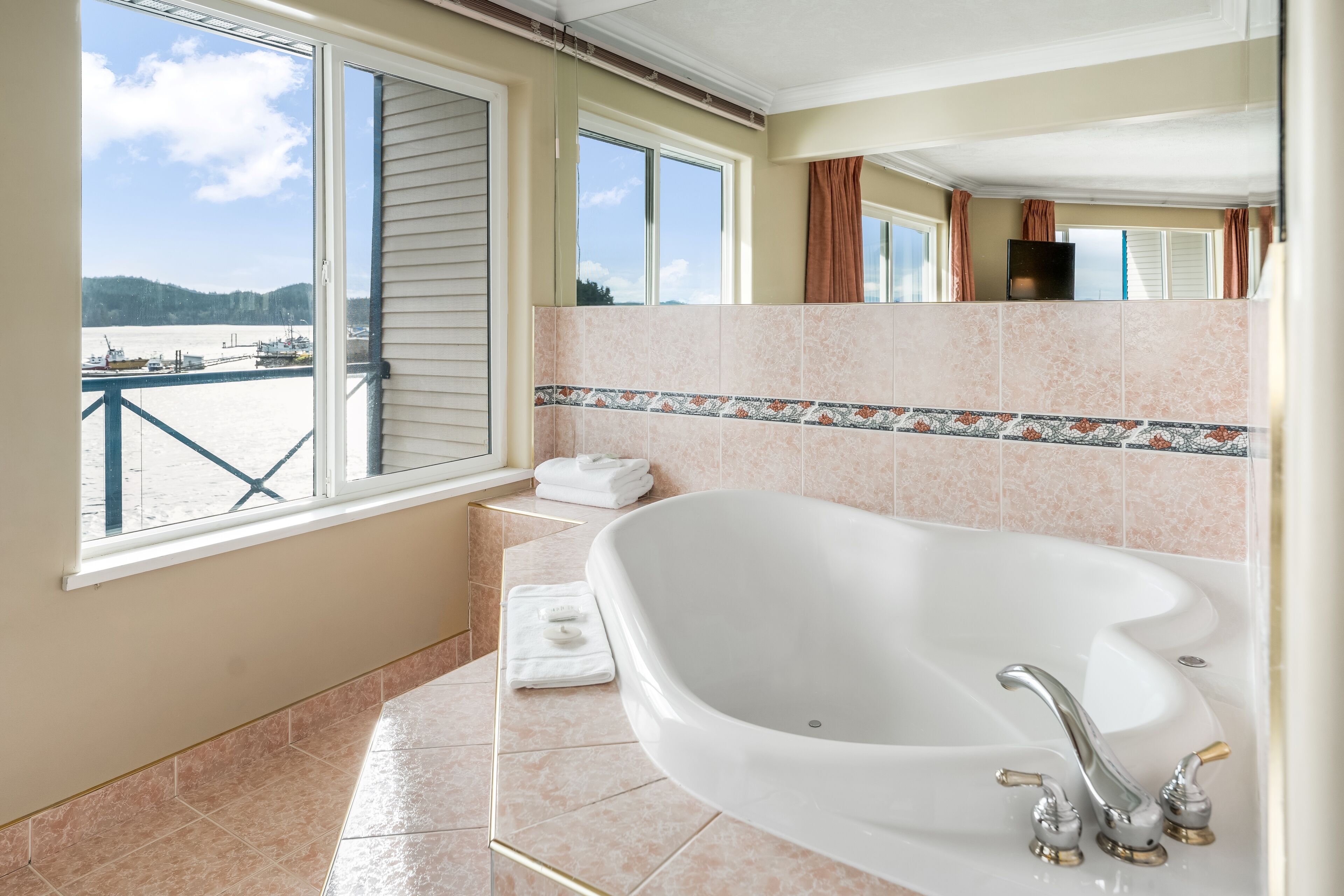 Un baño con una bañera grande, una ventana con vistas a una masa de agua y un salpicadero de azulejos.