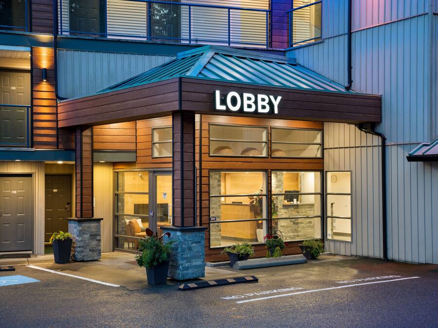 Un vestíbulo de hotel con un letrero que dice 'Lobby', ventanas amplias y plantas en macetas.