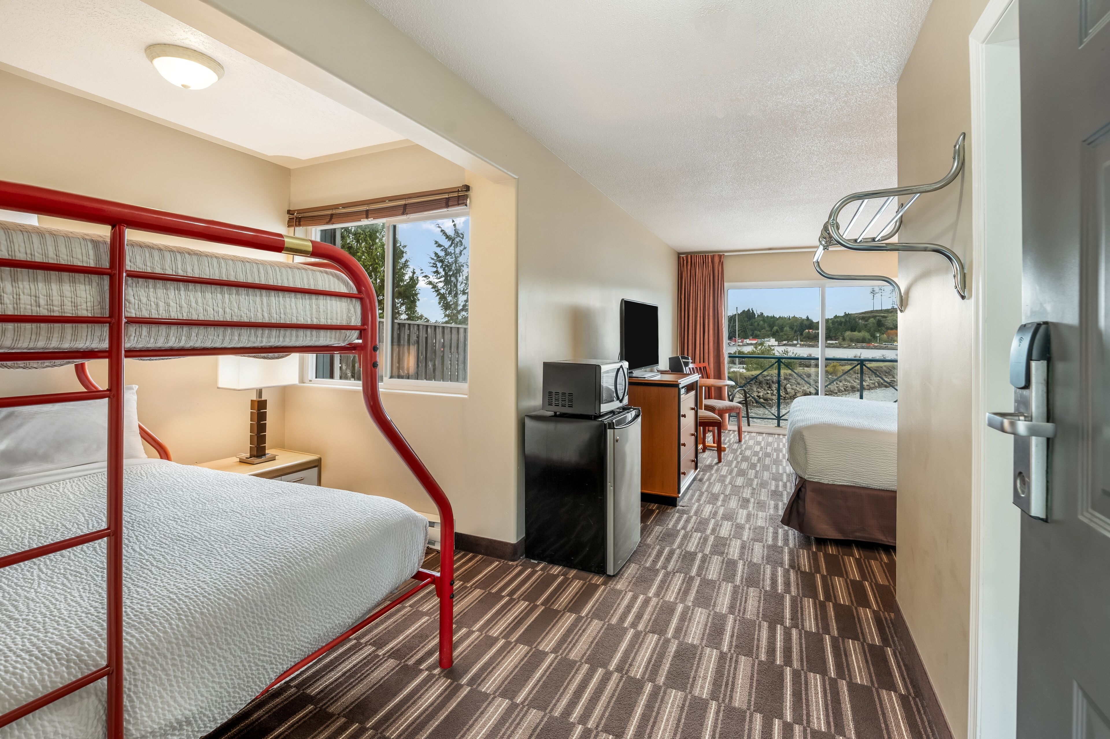 A hotel room with a bunk bed, desk, television, and a view of the outside.