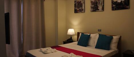 A hotel room with a bed, a nightstand, a lamp, and two paintings on the wall.