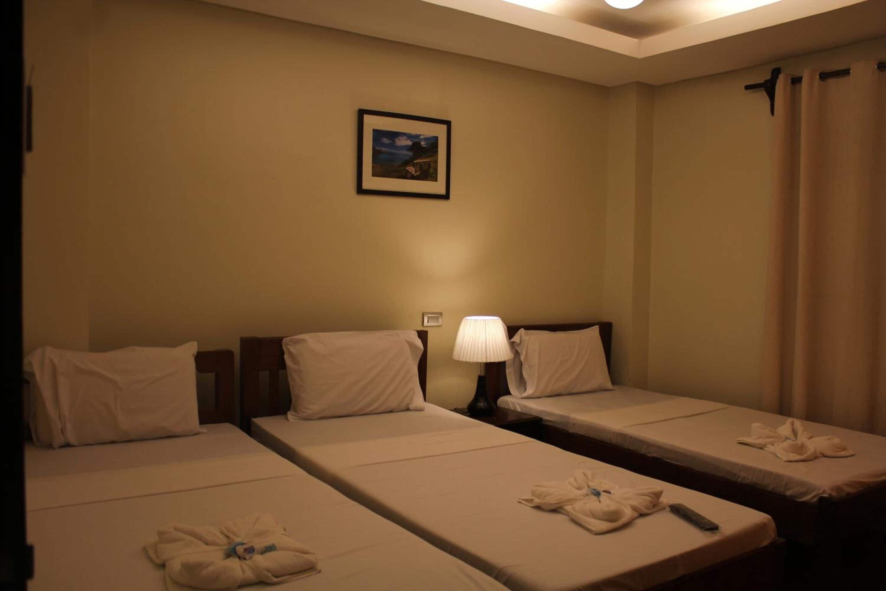 A hotel room with two single beds, a nightstand with a lamp, and a framed picture on the wall.