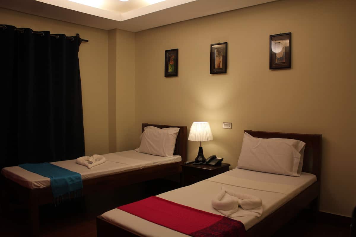 Zwei Einzelbetten mit weißen Laken, eine rote Decke auf einem Bett, ein hölzerner Nachttisch mit Lampe und ein schwarzes Telefon.